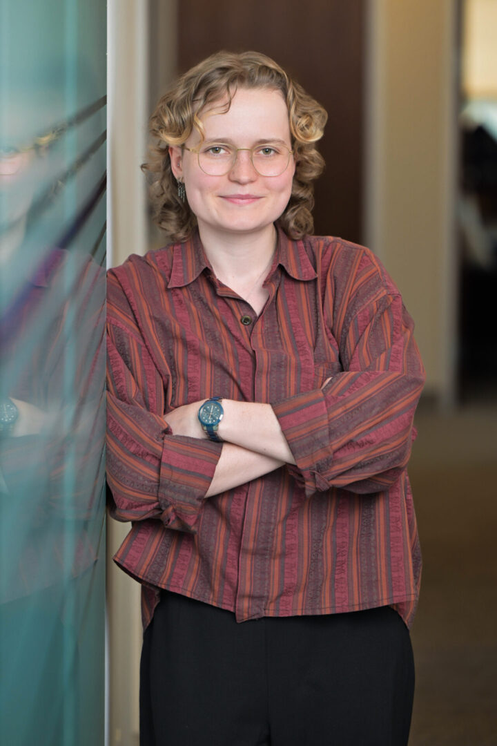 Person with glasses leaning against glass wall.