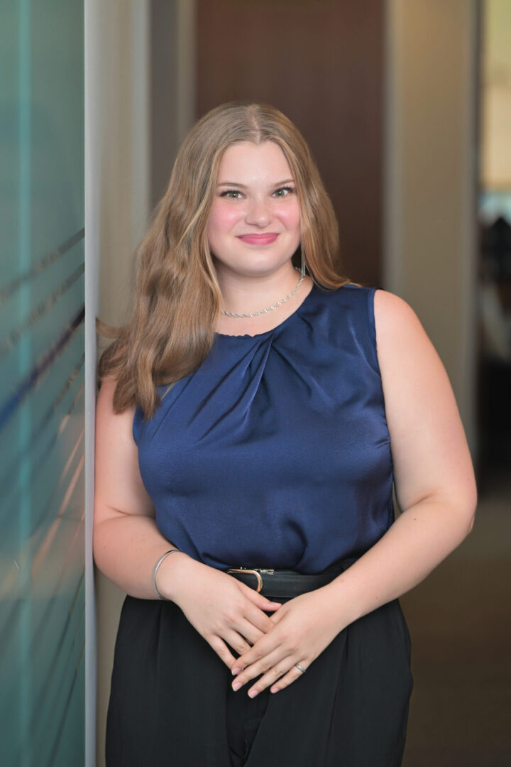 Smiling woman in blue blouse, standing indoors.