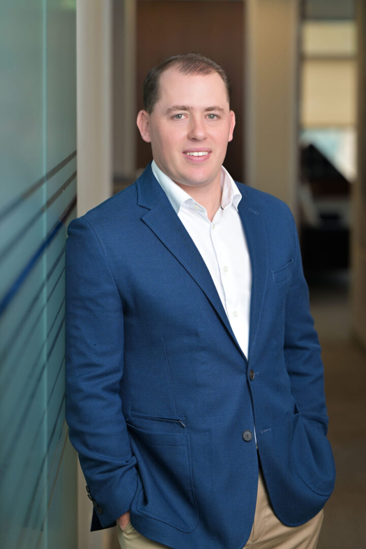 Man in blue suit leaning against wall.
