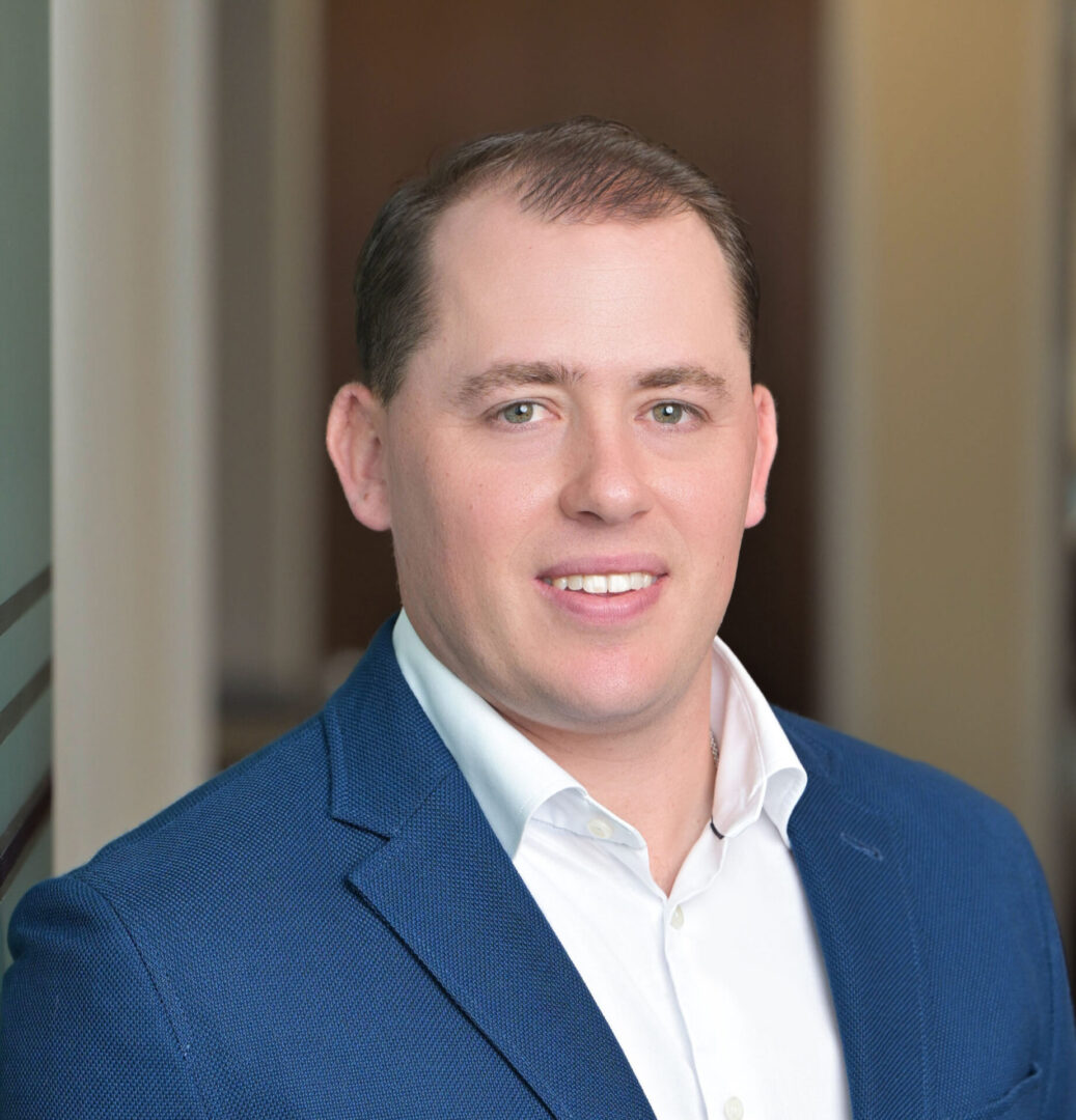 Man in blue suit smiling indoors.