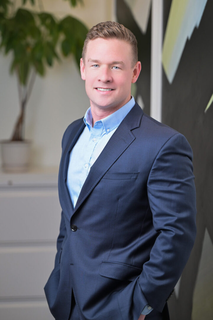 Man in blue suit, standing, smiling indoors.
